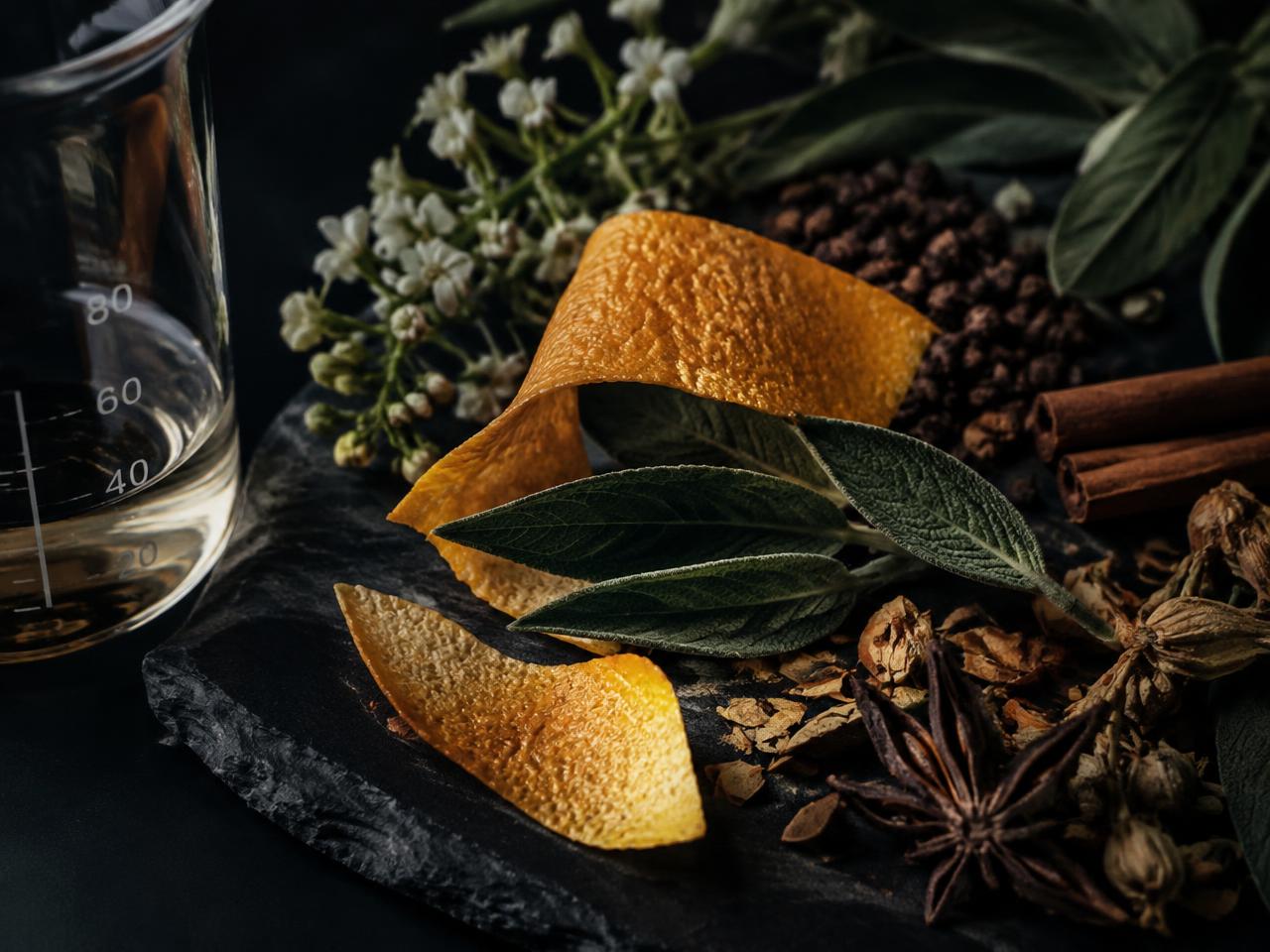 Citrus peel, sage and spices on black slate beside a glass beaker